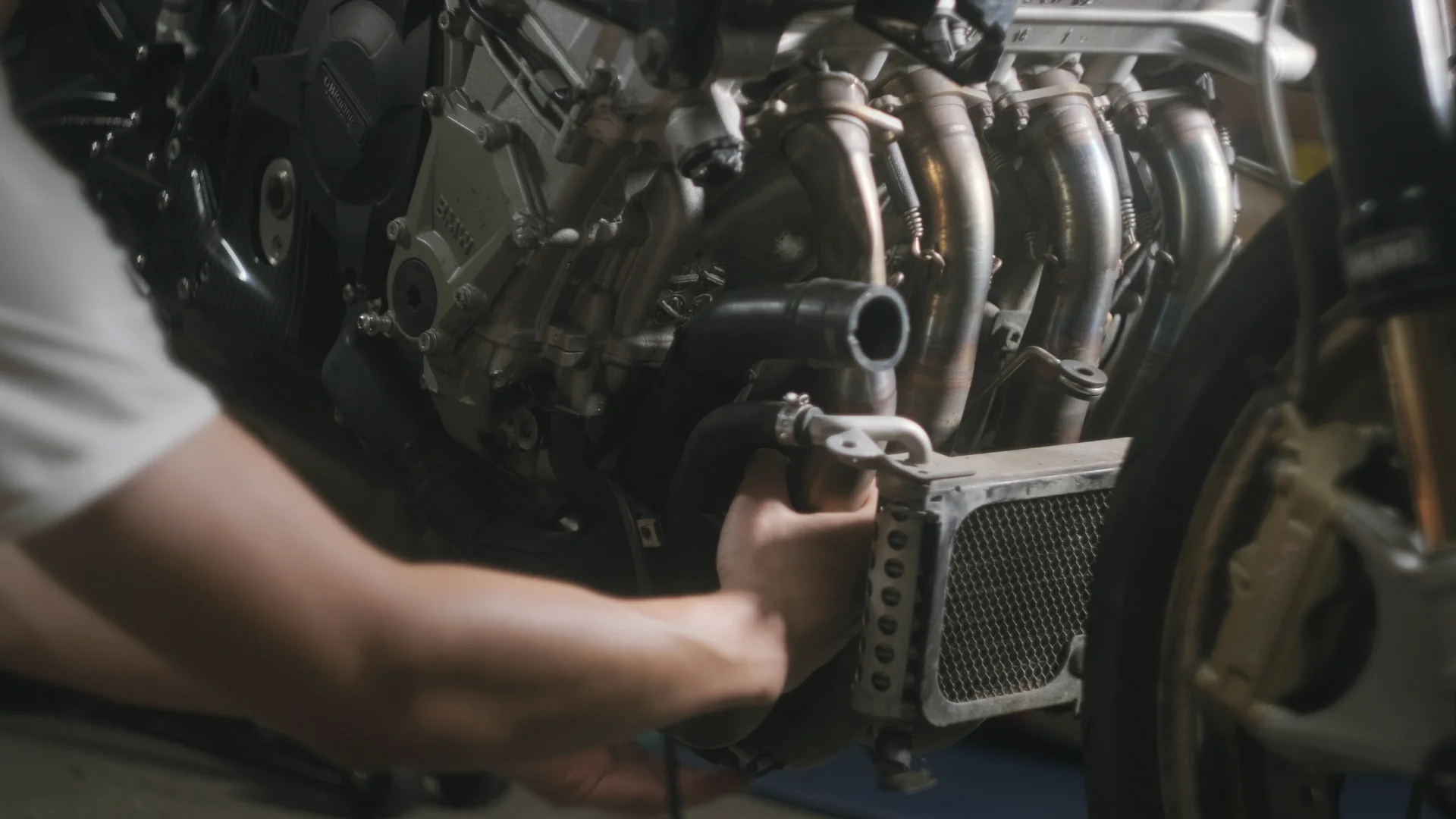 A hand holding a hose against the oil cooler, exhaust headers behind
