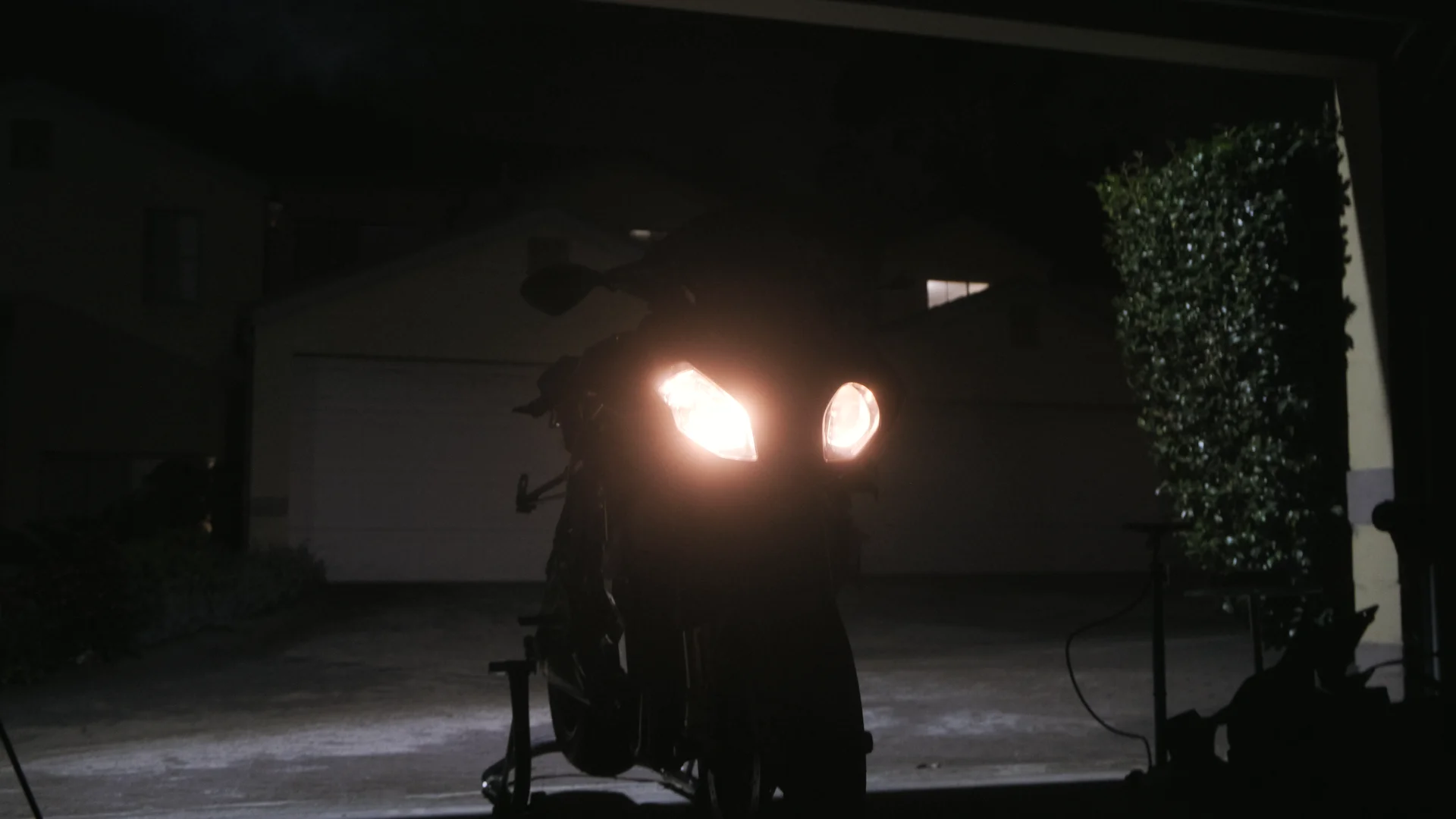 Motorcycle headlights lit in a garage doorway at night